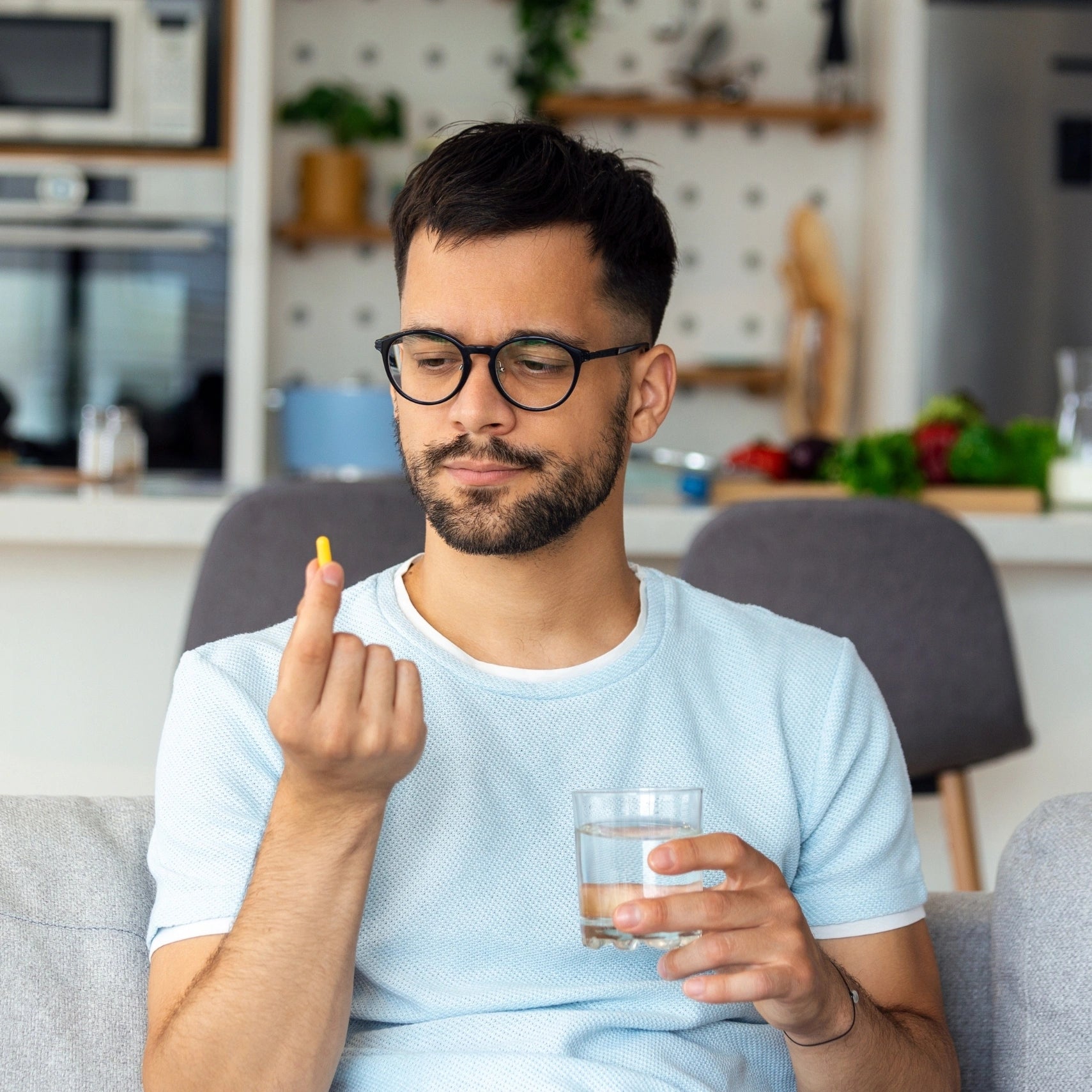 Man taking a pill with a glass of water against a plain background